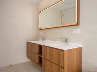 Modernes schwebendes Holzwaschtisch mit zwei integrierten Waschbecken und Chromarmaturen. Beleuchteter Spiegel mit Holzrahmen und strukturierte Wandfliesen.