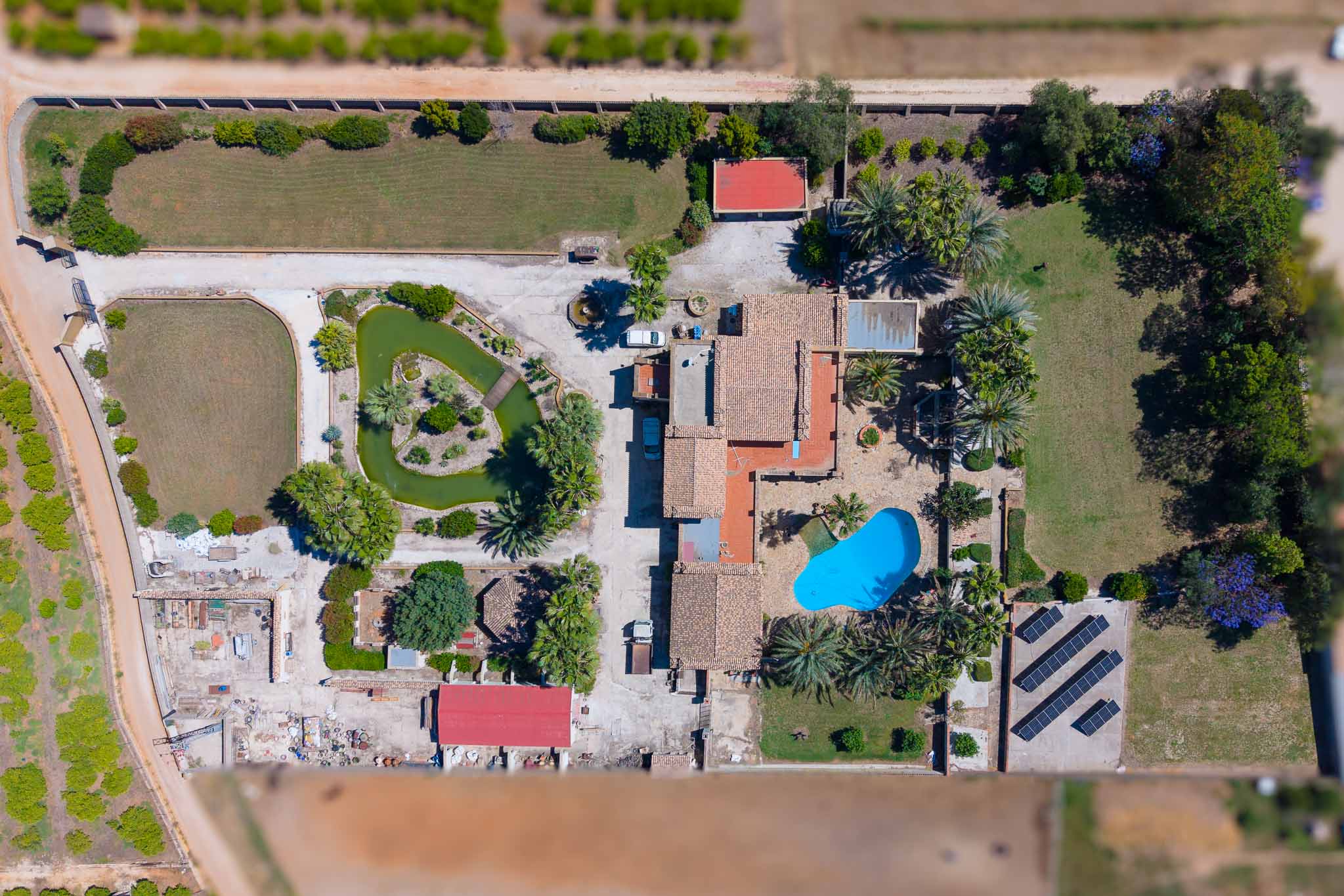 Detaillierte Luftaufnahme des weitläufigen Grundstücks, mit Hauptvilla, blauem Pool, Teich mit Insel und der Solaranlage.