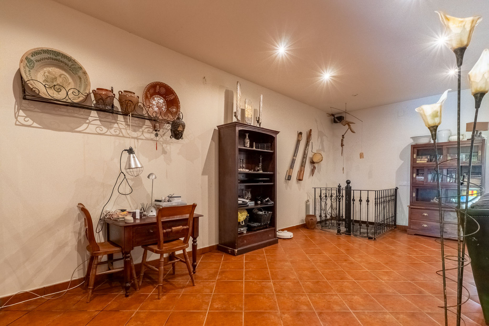 Funktionaler Arbeitsbereich mit Holzschreibtisch, Terrakotta-Bodenfliesen und traditioneller Wanddekoration. Der Raum umfasst ein Bücherregal und ein schmiedeeisernes Geländer.