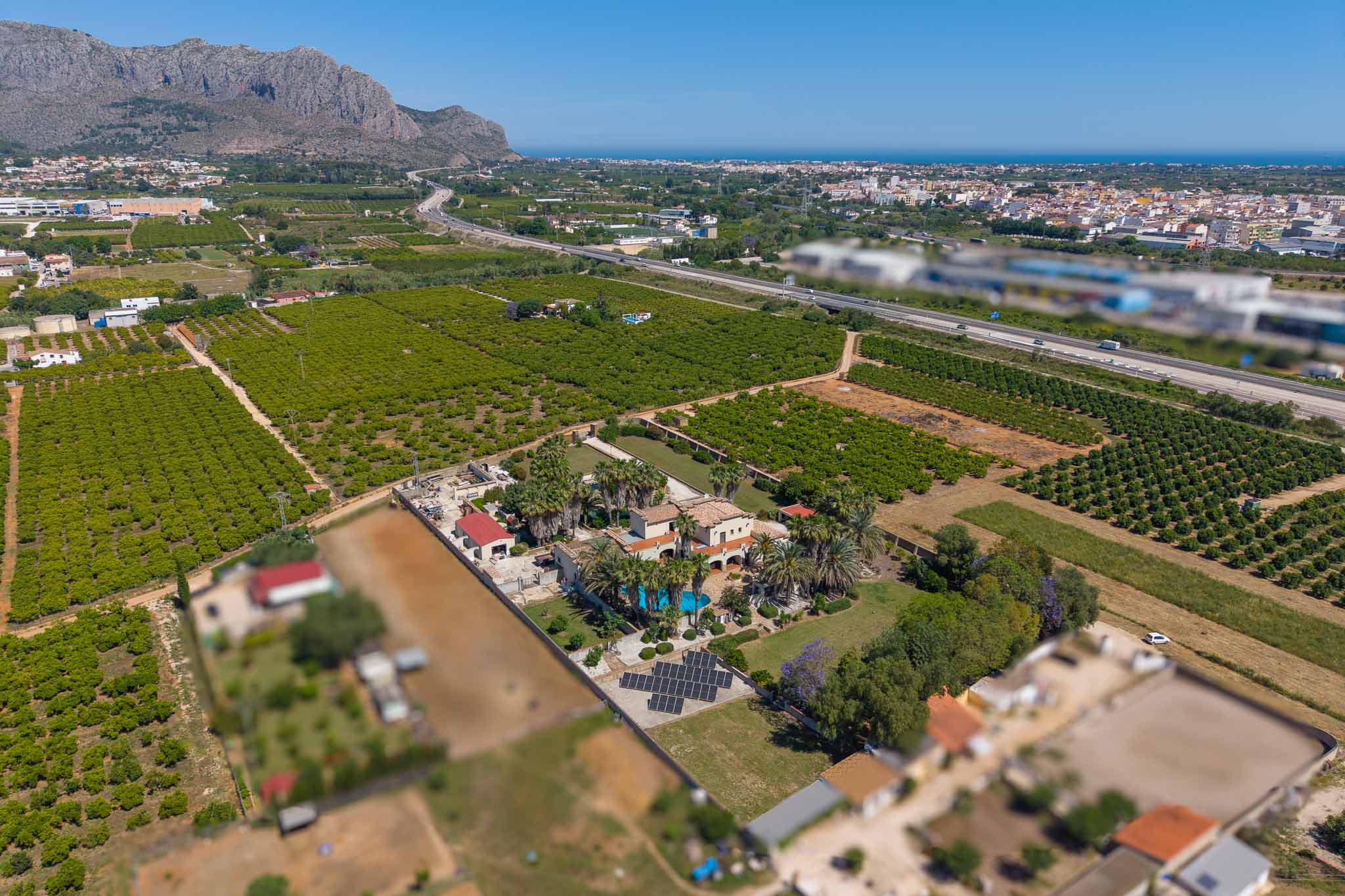 Luftaufnahme des Anwesens mit Haupthaus, Pool, weitläufigen Gärten und Solaranlage, umgeben von Orangenplantagen mit Meer- und Bergblick.