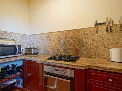 Ausgestattete Küchenecke mit Arbeitsplatten und Spritzschutz aus geädertem Granit, Einbaubackofen, Gasherd und dunklen Holzschränken. Offene Regale sind sichtbar.