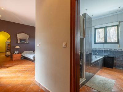 Blick vom Flur mit Terrakottafliesen, links ein Schlafzimmer mit dunklen Wänden und Zierspiegel, rechts ein gefliestes Badezimmer mit Badewanne.