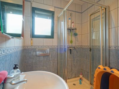 Funktionales Badezimmer mit Keramikwaschbecken, Glasduschkabine und blau-beigen Fliesen. Ein Fenster sorgt für natürliches Licht.