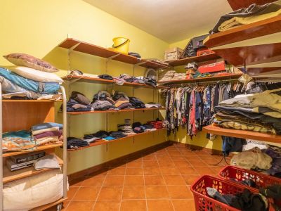 Geräumiger begehbarer Kleiderschrank mit offenen Holzregalen, hellgelben Wänden und Terrakottafliesenboden, ideal für umfassende Aufbewahrung.