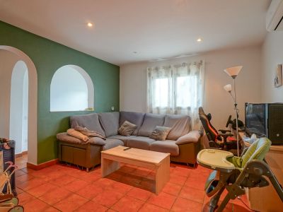 Geräumiger Wohnbereich mit grüner Akzentwand und Rundbögen, Terrakottafliesenboden und einem bequemen Ecksofa. Funktionale Gestaltung mit Tageslicht.