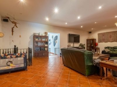 Geräumiger Wohnbereich mit Terrakotta-Fliesenboden, Einbauleuchten, dunklen Ledersofas und Holzvitrinen. Ein Wandfernseher und ein offener Zugang zum Treppenhaus sind sichtbar.