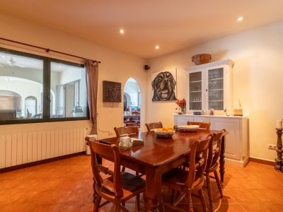 Geräumiges Esszimmer mit dunklem Holztisch und passenden Stühlen auf Terrakottafliesen. Der Raum verfügt über einen Heizkörper unter dem Fenster und einen weißen Vitrinenschrank.