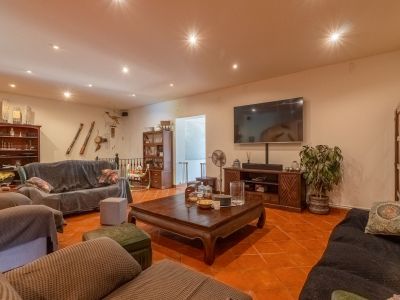 Geräumiges Wohnzimmer mit Terrakottafliesen, Deckenstrahlern und großem Wandfernseher. Dunkle Holzmöbel und überzogene Sofas schaffen ein einladendes Ambiente.