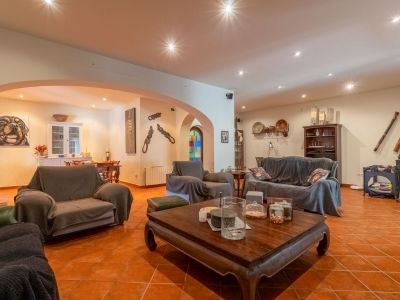 Geräumiges Wohnzimmer mit Terrakottafliesen und Deckeneinbaustrahlern. Es umfasst ein großes Sofa, Sessel und einen geschnitzten Holztisch, verbunden mit einem Essbereich durch Bögen.