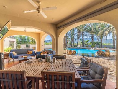 Großzügige überdachte Terrasse mit Bögen, ausgestattet mit Holz-Esstisch und Loungebereich, mit direktem Blick auf den Pool, Palmen und die Berglandschaft.