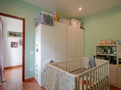 Kinderzimmer mit hellgrünen Wänden und Terrakottafliesenboden. Ausgestattet mit einem weißen Babybett, geräumigen weißen Kleiderschränken und einem Regal, beleuchtet durch Deckenstrahler.