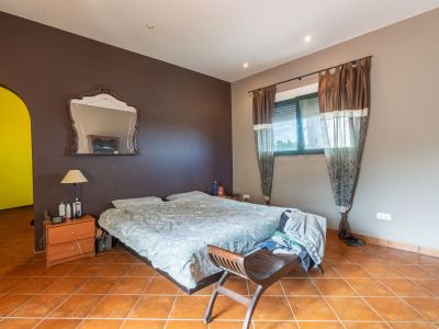 Schlafzimmer mit Doppelbett, Terrakottafliesen und zweifarbigen Wänden. Das Fenster mit Rollladen und Vorhängen sorgt für natürliches Licht.