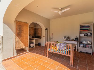 Überdachte Terrasse mit Terrakottafliesen und gemauertem Grill. Ausgestattet mit einer Holzsitzbank, Deckenventilator und Stauraum, ideal für Mahlzeiten im Freien.
