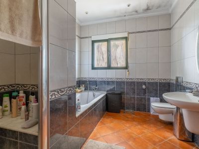 Voll ausgestattetes Badezimmer mit Terrakottafliesen, grauen Wandfliesen mit Zierbordüren, Badewanne, verglaster Dusche, Waschbecken und grün gerahmtem Fenster.