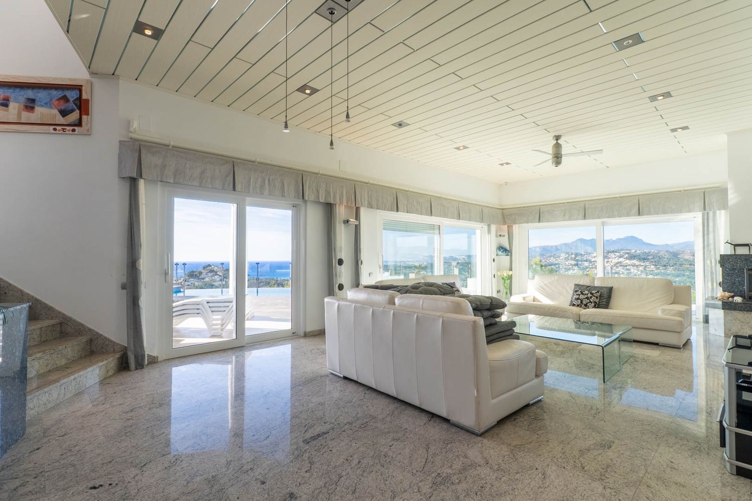 Geräumiges Wohnzimmer mit polierten Granitböden, Lamellendecken und Panoramablick auf Meer und Berge, direkter Zugang zur Terrasse und zum Pool.