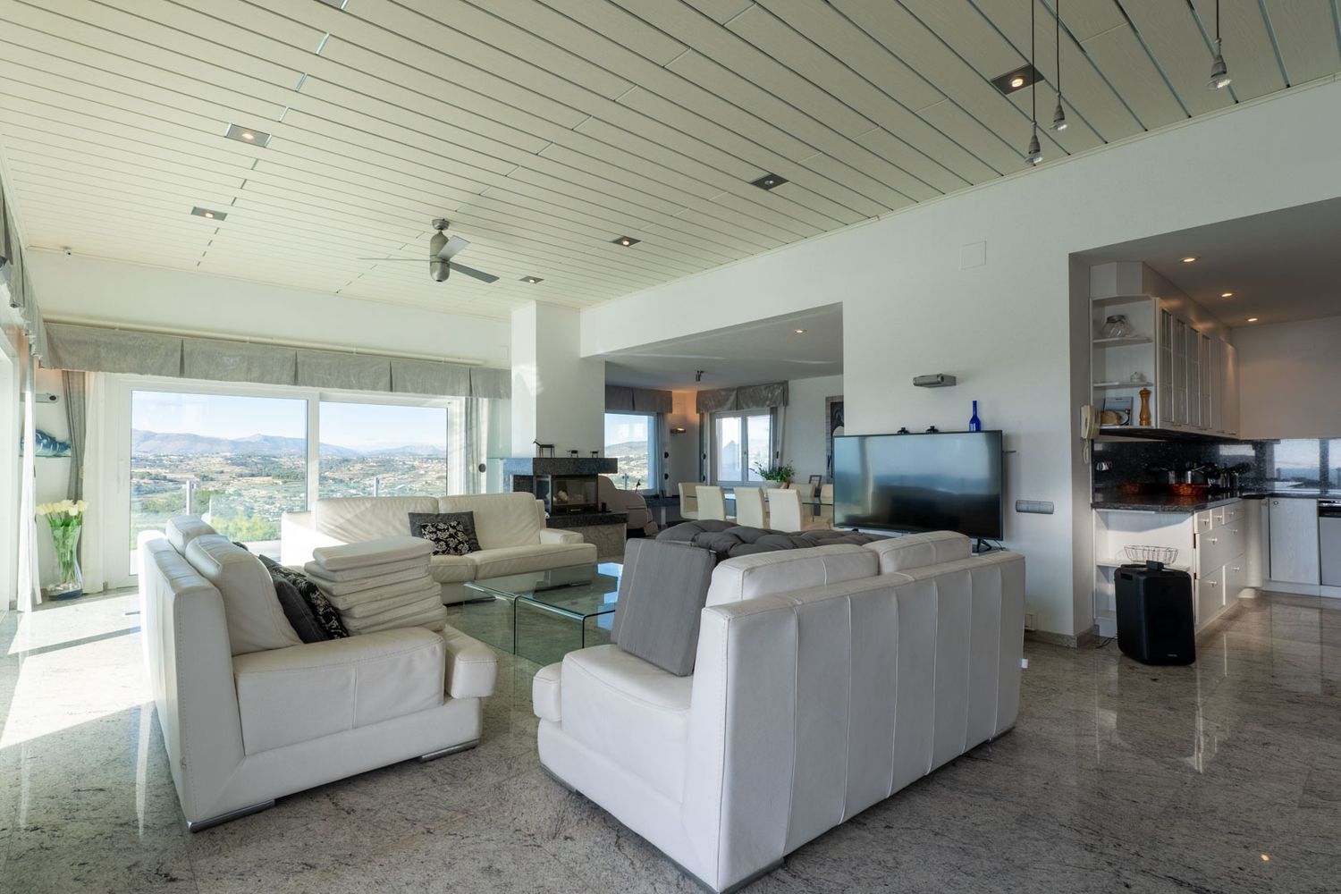 Heller Wohn-Essbereich mit weißen Ledersofas, Marmorboden und großen Fenstern mit Panoramablick auf die Berge. Die offene Küche verfügt über dunkle Granitarbeitsplatten.