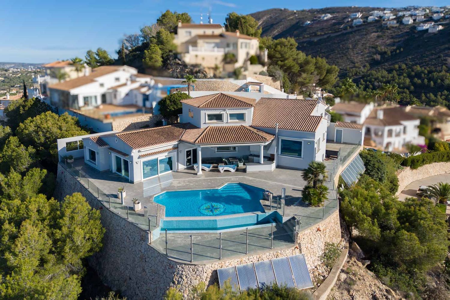 Luftaufnahme der Villa mit Infinity-Pool, Kompass-Mosaik und großzügiger Terrasse mit Glasgeländer. Charakteristisch sind die Ziegeldächer und Steinmauern in Hanglage.