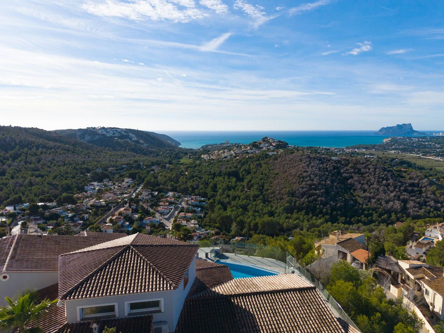 Luftaufnahme des Anwesens mit Terrakottadächern und Pool, eingebettet in grüne Hügel, mit Blick auf das Mittelmeer und den Peñón de Ifach in der Ferne.