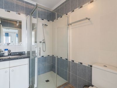 Badezimmer mit dunkler Granit-Waschtischplatte, dekorativem Spiegel und Glasduschkabine. Die Wände sind mit hellbeigen und blau-grauen Fliesen sowie einer Mosaikbordüre versehen.