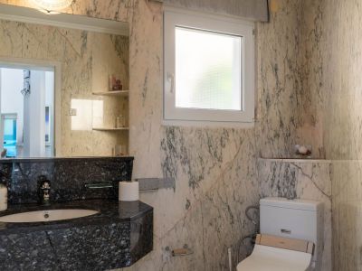 Badezimmer mit hellen, geäderten Marmorwänden, einem dunklen Granitwaschtisch mit integriertem Waschbecken und einem großen Spiegel. Ein Milchglasfenster und eine Toilette mit Bidetfunktion sind vorhanden.
