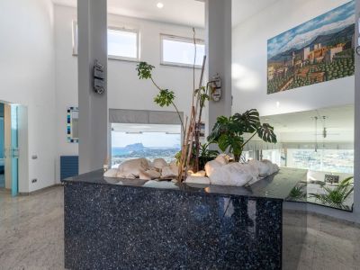 Eingangshalle mit dunkler Granitinsel, weißen Steinen und Pflanzen. Hohe Decken und große Fenster bieten Panoramablick auf das Meer und den Peñón de Ifach.