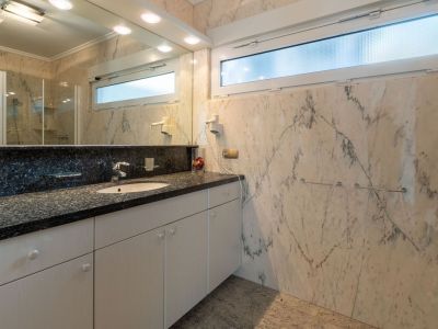Elegantes Badezimmer mit Wänden und Boden aus geädertem Marmor. Der Waschtisch verfügt über eine dunkle Granitarbeitsplatte und ein integriertes Waschbecken, ergänzt durch ein mattiertes Oberlicht.