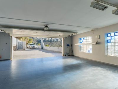 Geräumige Garage mit hellblauem Fliesenboden und Glasbausteinfenstern mit blauen Akzenten, das Tor öffnet sich zur Auffahrt und den entfernten Hügeln.