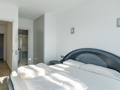 Helles Schlafzimmer mit Doppelbett und dunklem Holzkopfteil mit geflochtener Einlage. Es verfügt über einen Einbauschrank und direkten Zugang zu einem Bad mit Glasdusche.
