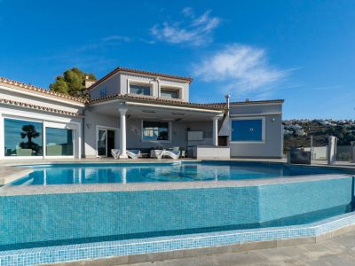 Infinity-Pool mit blauen Mosaikfliesen und überdachte Terrasse mit Außenküche, direkt an der Villenfassade.