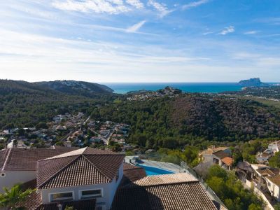 Luftaufnahme des Anwesens mit Terrakottadächern und Pool, eingebettet in grüne Hügel, mit Blick auf das Mittelmeer und den Peñón de Ifach in der Ferne.