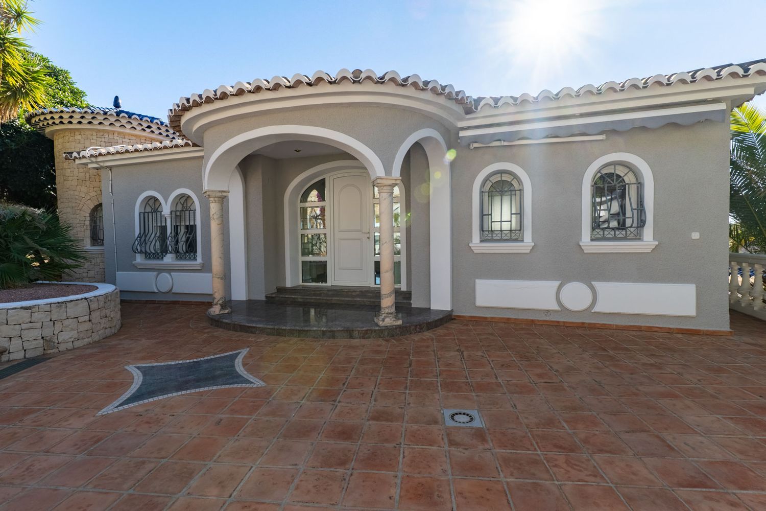 Haupteingang der Villa mit geschwungener Veranda, Marmorsäulen und weißen Bögen. Rundbogenfenster mit schmiedeeisernen Gittern und Terrakotta-Pflasterung.
