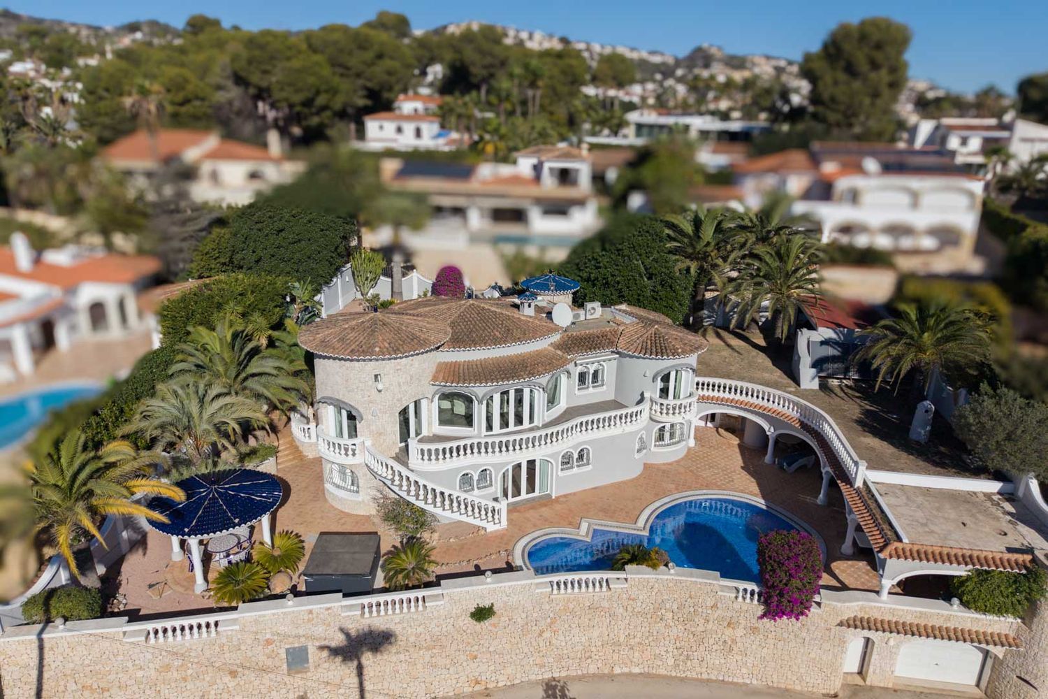 Luftaufnahme der Luxusvilla mit ihrer markanten Architektur, privatem Pool, mehreren Terrassen mit weißen Balustraden und üppigem mediterranem Garten.