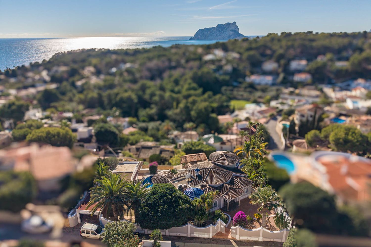 Luftaufnahme der Villa mit ihren markanten Ziegeldächern, eingebettet in üppige mediterrane Gärten. Im Hintergrund erstreckt sich der Panoramablick auf das Meer und den Peñón de Ifach.