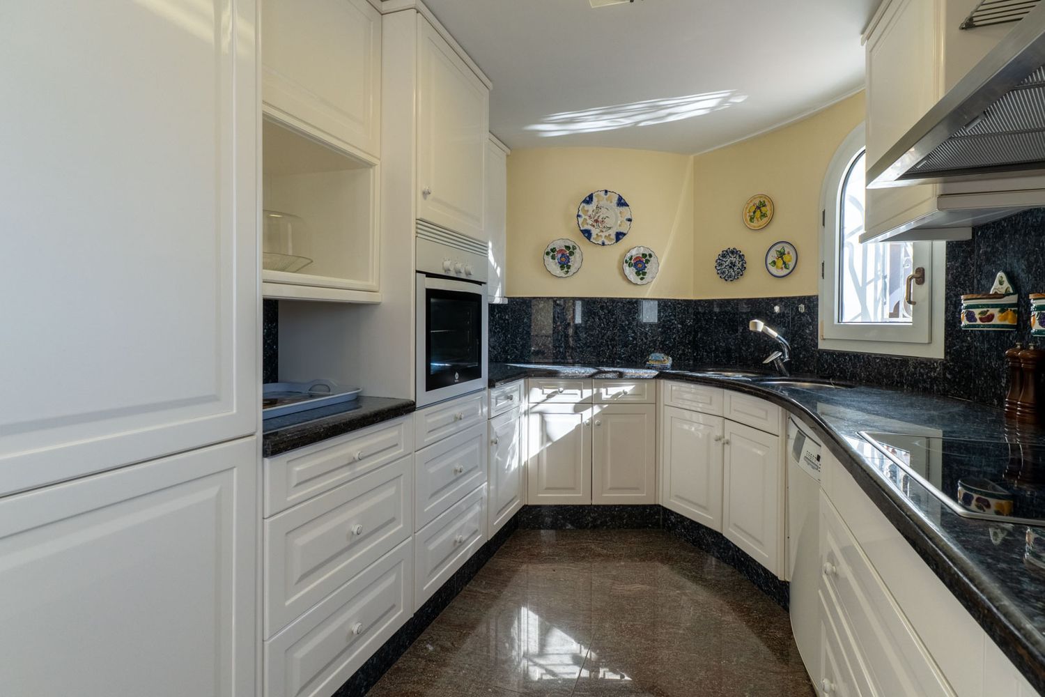 Separate Küche mit weißen Schränken, dunklen Granitarbeitsplatten und Spritzschutz. Sie verfügt über einen Einbaubackofen, Spüle und ein gewölbtes Fenster für Tageslicht.