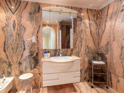 Badezimmer mit auffälligem rosa Marmor und dunklen Adern, ausgestattet mit einem schwebenden Waschtisch, beleuchtetem Spiegelschrank und Bidet.