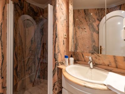 Badezimmer mit markanten rosa-schwarz geäderten Marmorwänden, einem weißen Keramikwaschbecken und einer Glasduschkabine mit Chromarmatur.
