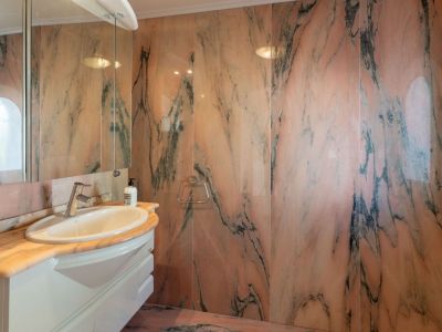 Elegantes Badezimmer mit Wänden und Waschtischplatte aus markantem rosa Marmor mit dunklen Adern. Ein weißer Waschtisch mit ovalem Becken und Spiegelschrank bietet Funktionalität.