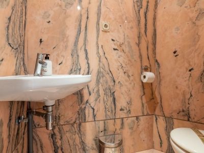 Gäste-WC mit Wänden und Boden aus rosa geädertem Marmor. Ausgestattet mit einem wandmontierten weißen Waschbecken, Chromarmatur und Toilette.