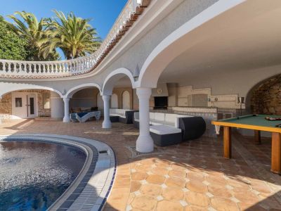 Große überdachte Terrasse mit geschwungenem Pool, Außenküche, Loungebereich und Billardtisch auf Terrakottafliesen.