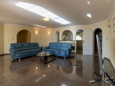 Großzügiger Wohnbereich mit dunklem, poliertem Marmorboden, blauen Ledersofas und mehreren Rundbögen zu angrenzenden Räumen. Natürliches Licht spiegelt sich an der Decke.