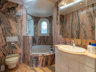 Hauptbadezimmer mit rosa-schwarz geädertem Marmor, einer eingebauten Badewanne in einer Rundnische und einem Bogenfenster.