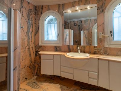 Hauptbadezimmer mit Wänden und Boden aus geädertem rosa Marmor, einem schwebenden weißen Waschtisch mit integriertem Waschbecken und zwei gewölbten Milchglasfenstern.