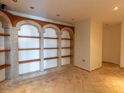 Innenraum mit Terrakotta-Bodenfliesen und gemauertem Regal mit Ziegelbögen und Holzbrettern. Einbaustrahler und eine markante Ecke mit rundem Bodendetail.