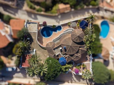 Luftaufnahme der Villa mit gestuften Terrakotta-Ziegeldächern, einem unregelmäßig geformten Privatpool und einer Terrakotta-Terrasse. Umgeben von Palmen und mediterraner Vegetation.