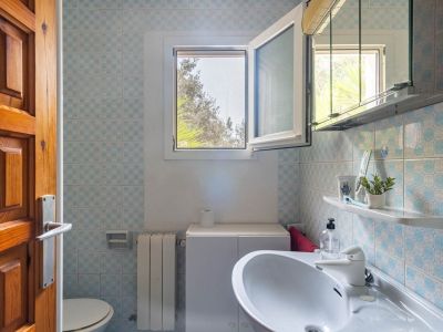 Badezimmer mit blau-weiß gemusterten Fliesen, Waschbecken mit Unterschrank und offenem Fenster, das natürliches Licht und Blick ins Grüne bietet.
