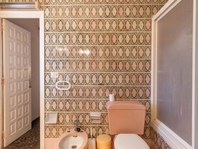 Badezimmer mit grün-beigen gemusterten Fliesen, rosa Toilette und Bidet, Milchglas-Duschwand und gesprenkeltem Terrazzoboden.