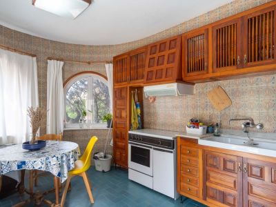 Funktionale Küche mit traditionellen Holzschränken, gemusterten Wandfliesen und einem Rundbogenfenster. Ein Essbereich mit rundem Tisch erhält natürliches Licht.