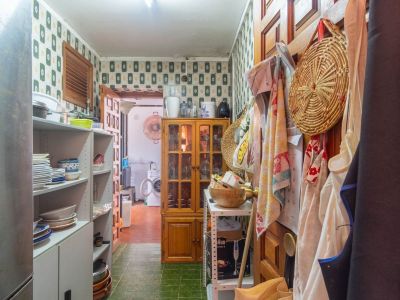 Funktionaler Hauswirtschaftsbereich mit gemusterter Tapete, grünem Fliesenboden, offenen Regalen für Geschirr und einem Holzvitrinenschrank. Waschbereich im Hintergrund erkennbar.