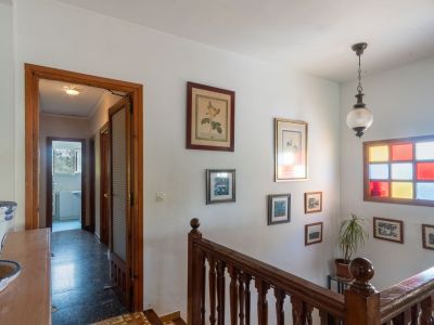 Heller Flur mit klassischer Holztreppe und Geländer. Ein markantes Buntglasfenster und gerahmte Bilder schmücken die weiße Wand.