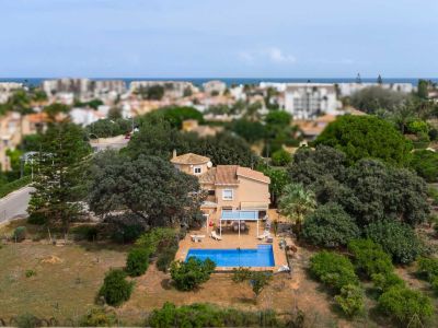Luftaufnahme der Villa mit blauem Pool, schattiger Terrasse und großem, bewachsenem Garten. Im Hintergrund sind die Stadtkulisse und das Mittelmeer erkennbar.